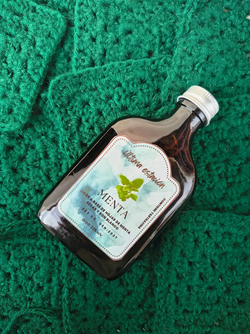 Botella de licor artesanal de menta de Última Estación sobre un tejido verde al crochet